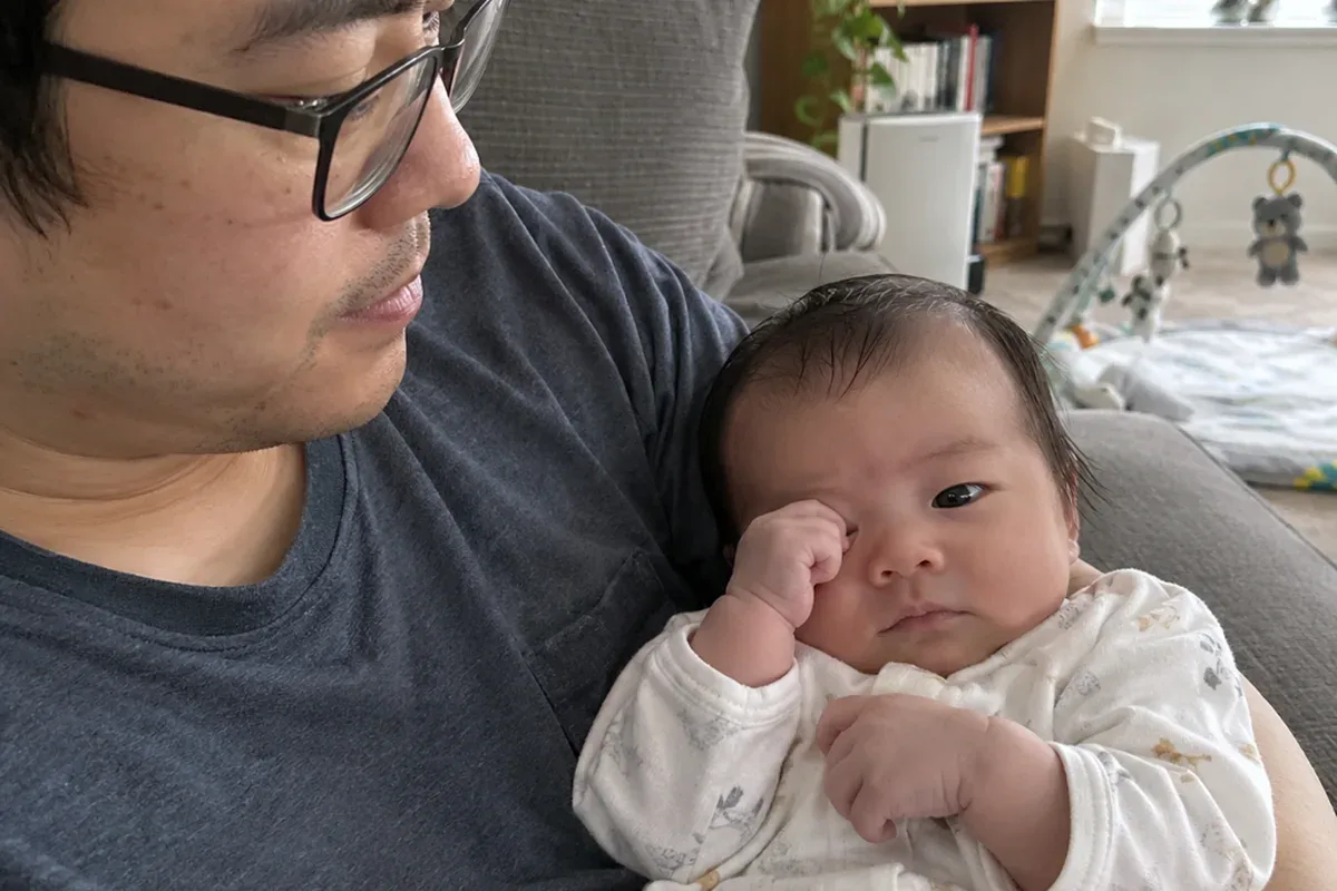 A 1 month old in a parent's arms yawning wide and looking away from the parent