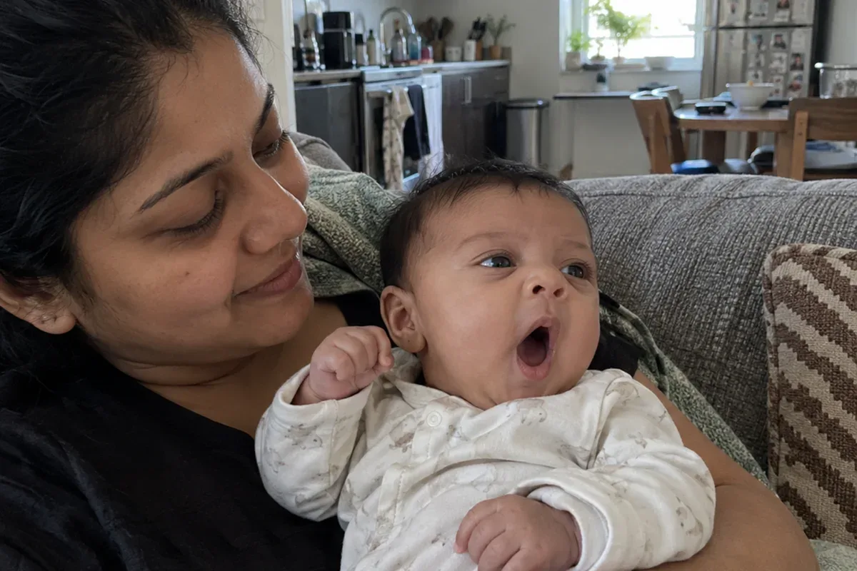 A 2 month old in a parent's arms yawning and looking away from a toy the parent is holding