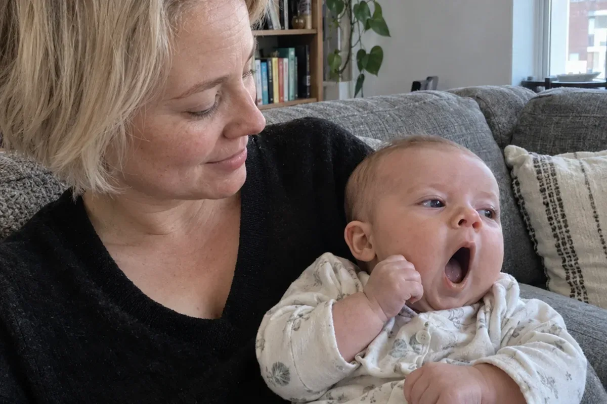 A 4 month old in a parent's arms rubbing one eye and staring into the distance