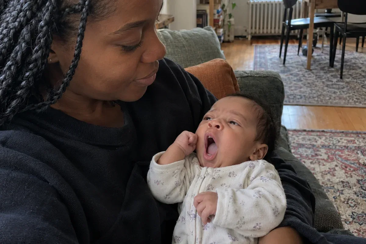 A 6 week old resting in a parent's arms, rubbing one eye and staring off to the side