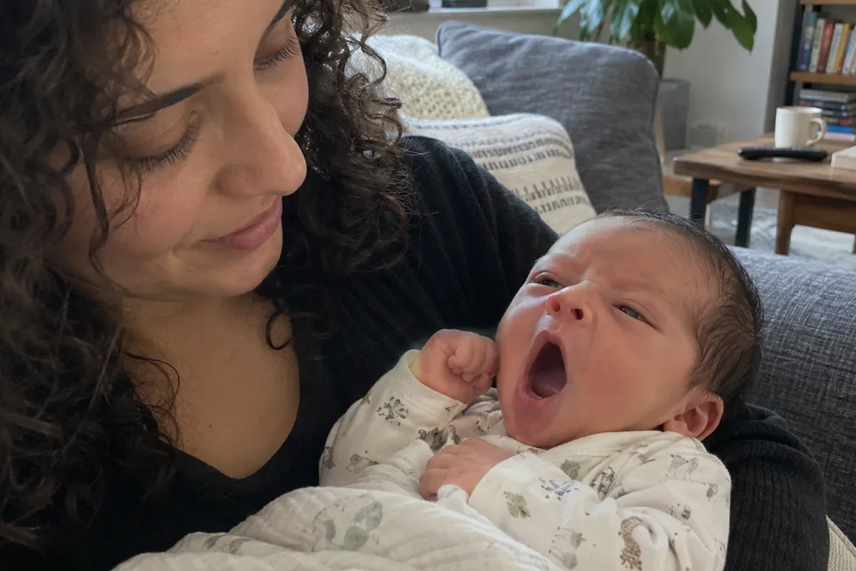 A newborn in a parent's arms yawning and turning their face away from the camera
