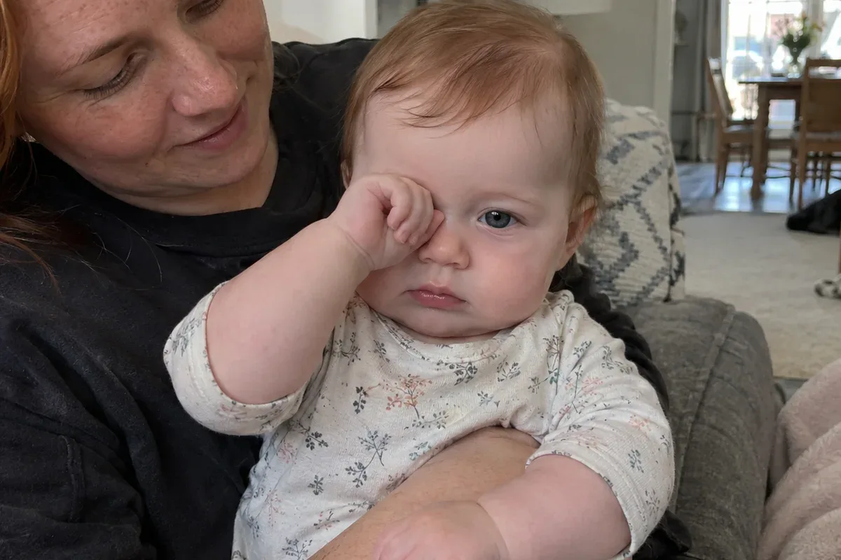 Close photo of a 7 month old in a parent's arms, yawning and looking away from the room