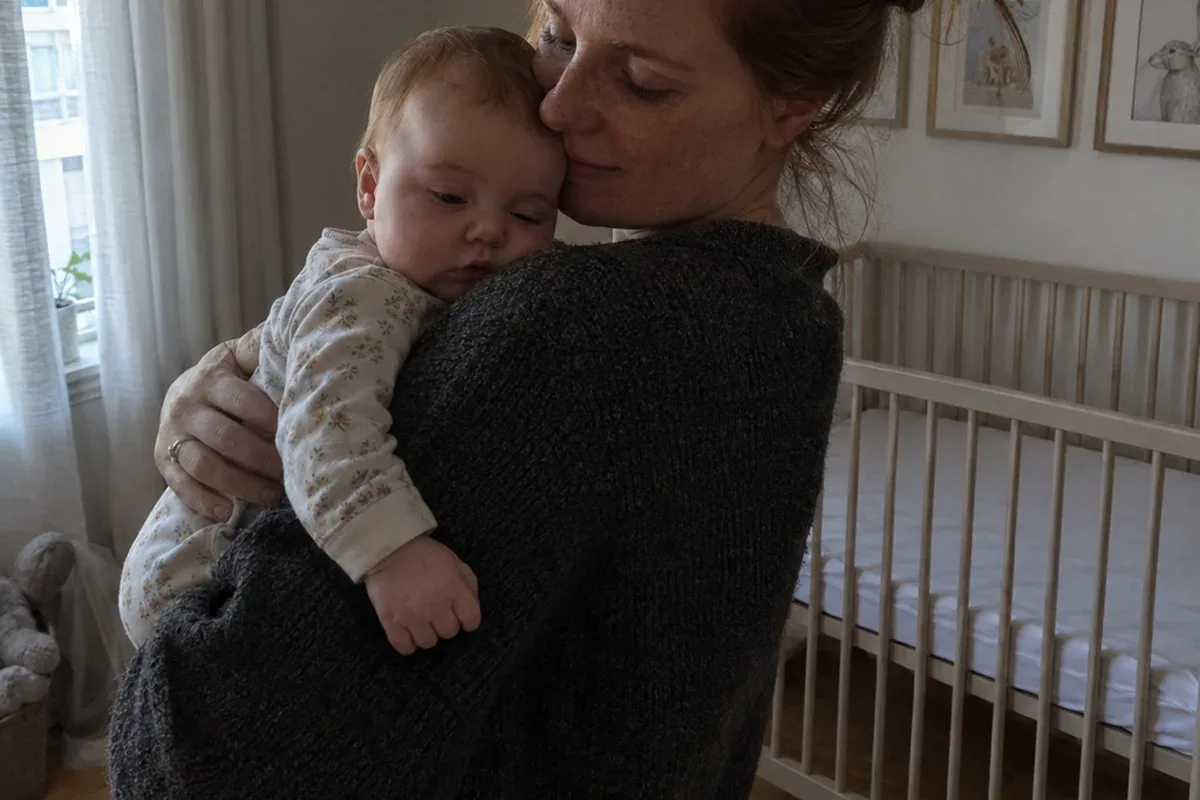 Parent in a dim nursery swaying with a drowsy, awake 7 month old on their shoulder, empty crib behind them