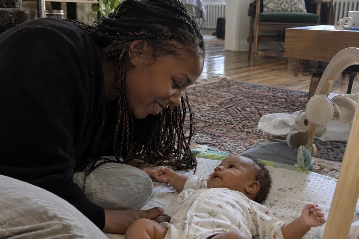 Parent kneeling beside a 6 week old doing tummy time on a play mat, the baby lifting their head briefly