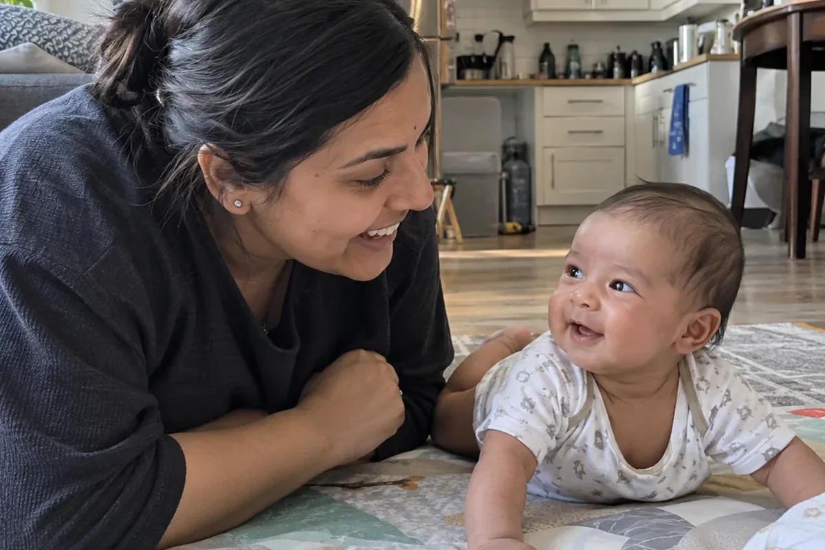 Parent lying on a play mat face to face with a 2 month old during tummy time, both smiling